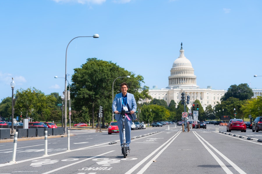 A man on a scooter in front of the capitol looking happy