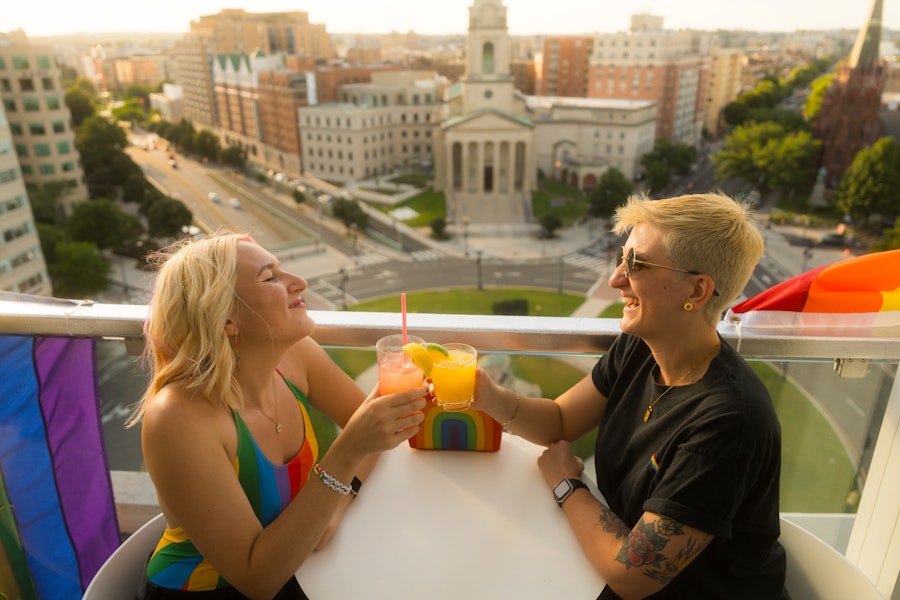 A couple enjoying a cocktail on a rooftop with a view of historic city buildings below. 
