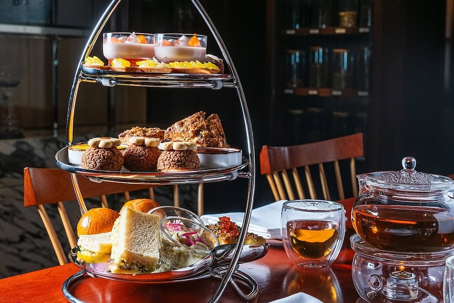 A modern, three-tiered tea set filled with hearty pastries and sandwiches in a rustic setting. 