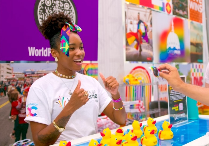 A young woman with a rainbow bow in her hair plays a game with an attendee at an event booth.