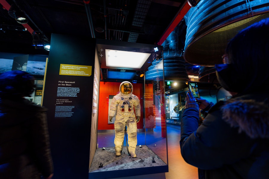 A visitor takes a photo of Neil Armstrong’s Apollo 11 spacesuit on display behind glass.