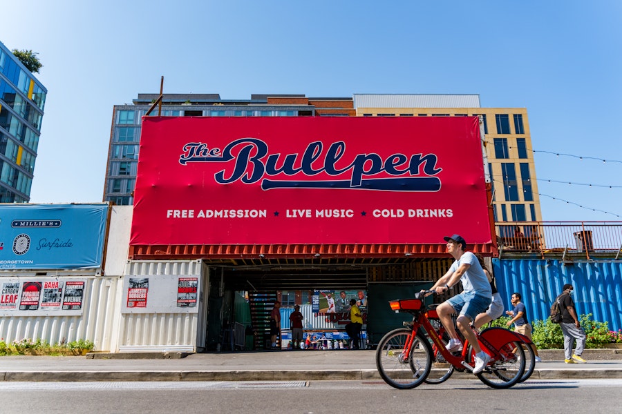 A cyclist rides past The Bullpen, an open-air venue near Nationals Park advertising live music, cold drinks and free admission.