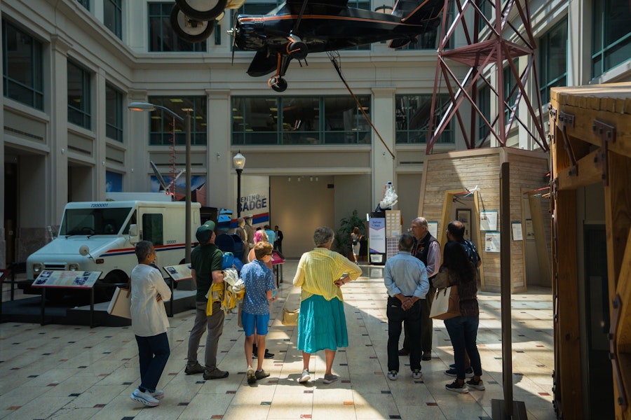 A tour group observes historic mail vehicles and aircraft inside the Smithsonian National Postal Museum.