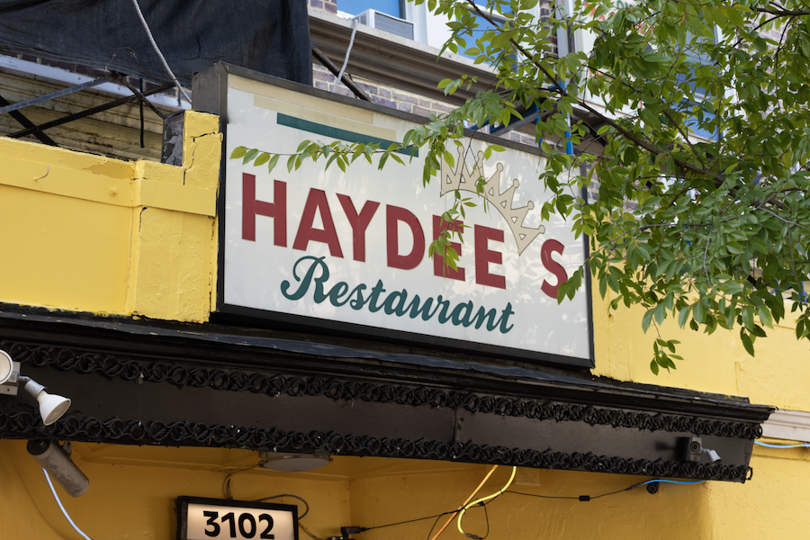 The red and green Haydee’s Restaurant sign is mounted above a bright yellow building facade.