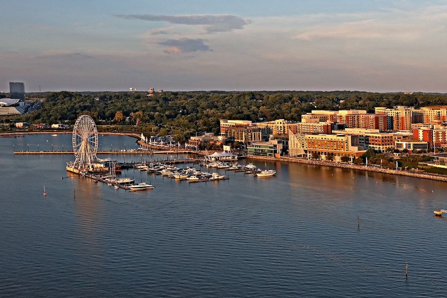 An aerial view of National Harbor at sunset, featuring the Capital Wheel, marina and waterfront hotels along the Potomac River.