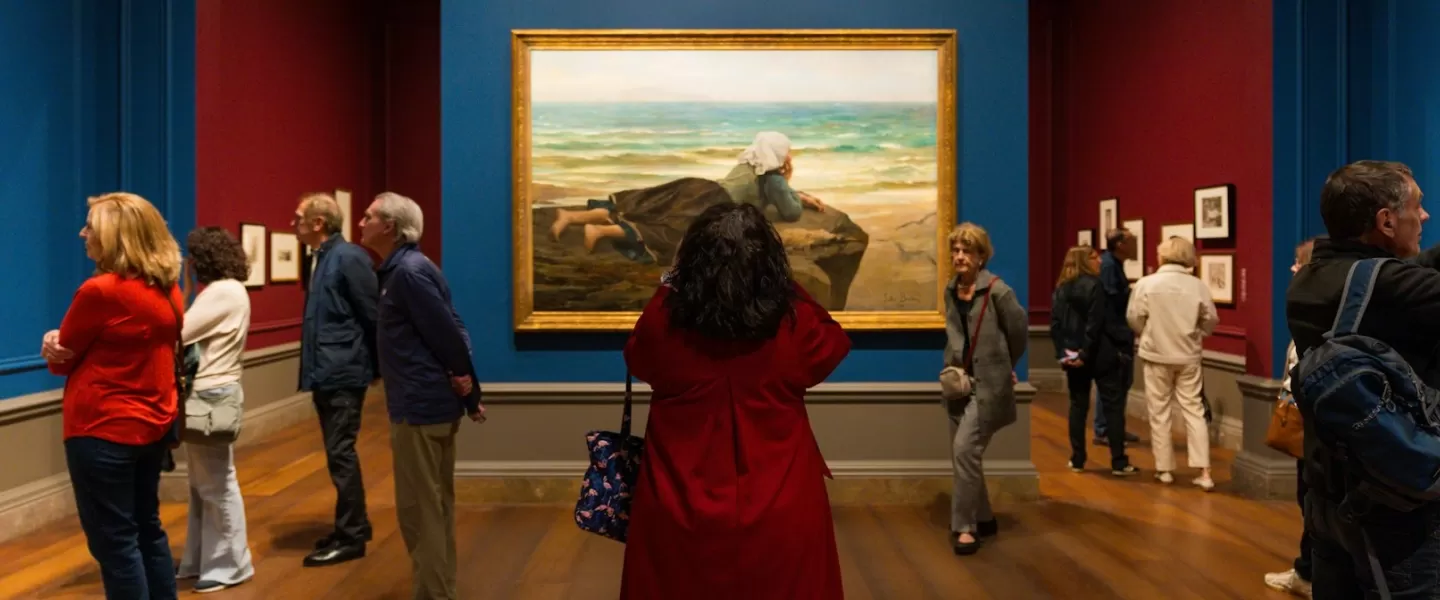 Visitors admire a large framed painting in a richly colored gallery at the National Gallery of Art.