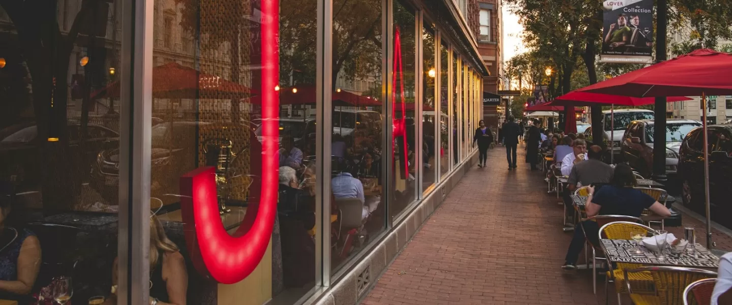 The exterior of Jaleo by José Andrés in Washington, DC, with large red neon lettering and outdoor seating under red umbrellas.