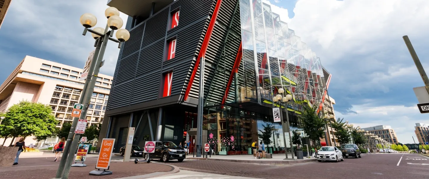 The modern glass and steel exterior of the International Spy Museum in Washington, DC, featuring red architectural accents and pedestrians along the street.