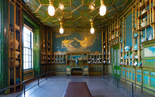 The Peacock Room at the Freer Gallery decorated with blue-green walls, gold accents and porcelain displays.
