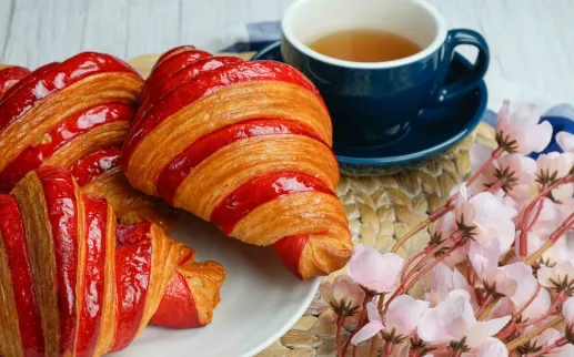 A table with quiche, sandwich, raspberry croissant, dessert, cherries and coffee.