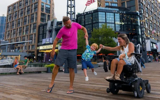 Parents hold their child's hands and swing him in the air as they enjoy a day on the Wharf. 
