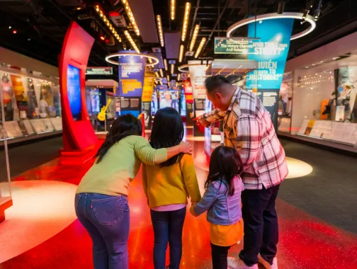 A family explores a vibrant museum exhibit together, with the father pointing toward a display as the children look on in curiosity.