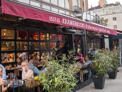 Diners enjoy outdoor seating at Kramerbooks & Afterwords Café in Dupont Circle as pedestrians stroll past the bustling sidewalk café.