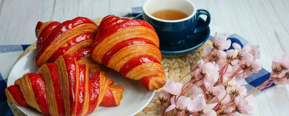 A table with quiche, sandwich, raspberry croissant, dessert, cherries and coffee.
